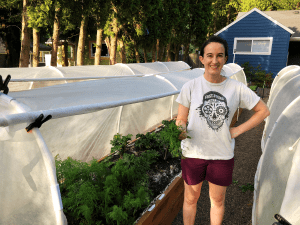 Sarah from Till Next Time Farms stands in front of a raised bed with a handful of dill