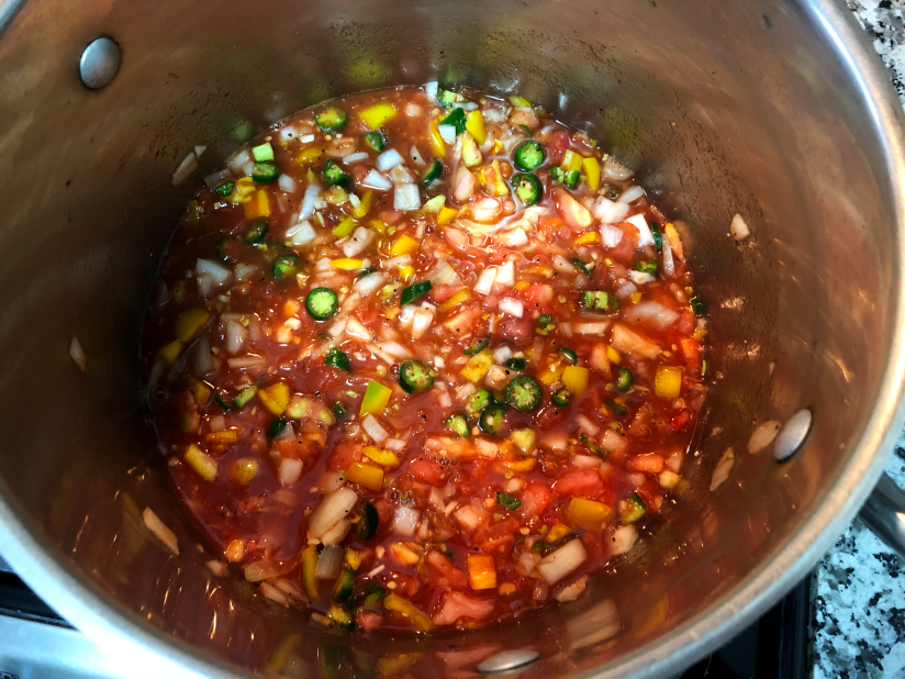 Red tomato salsa in a stainless steel pot with peppers and onions.
